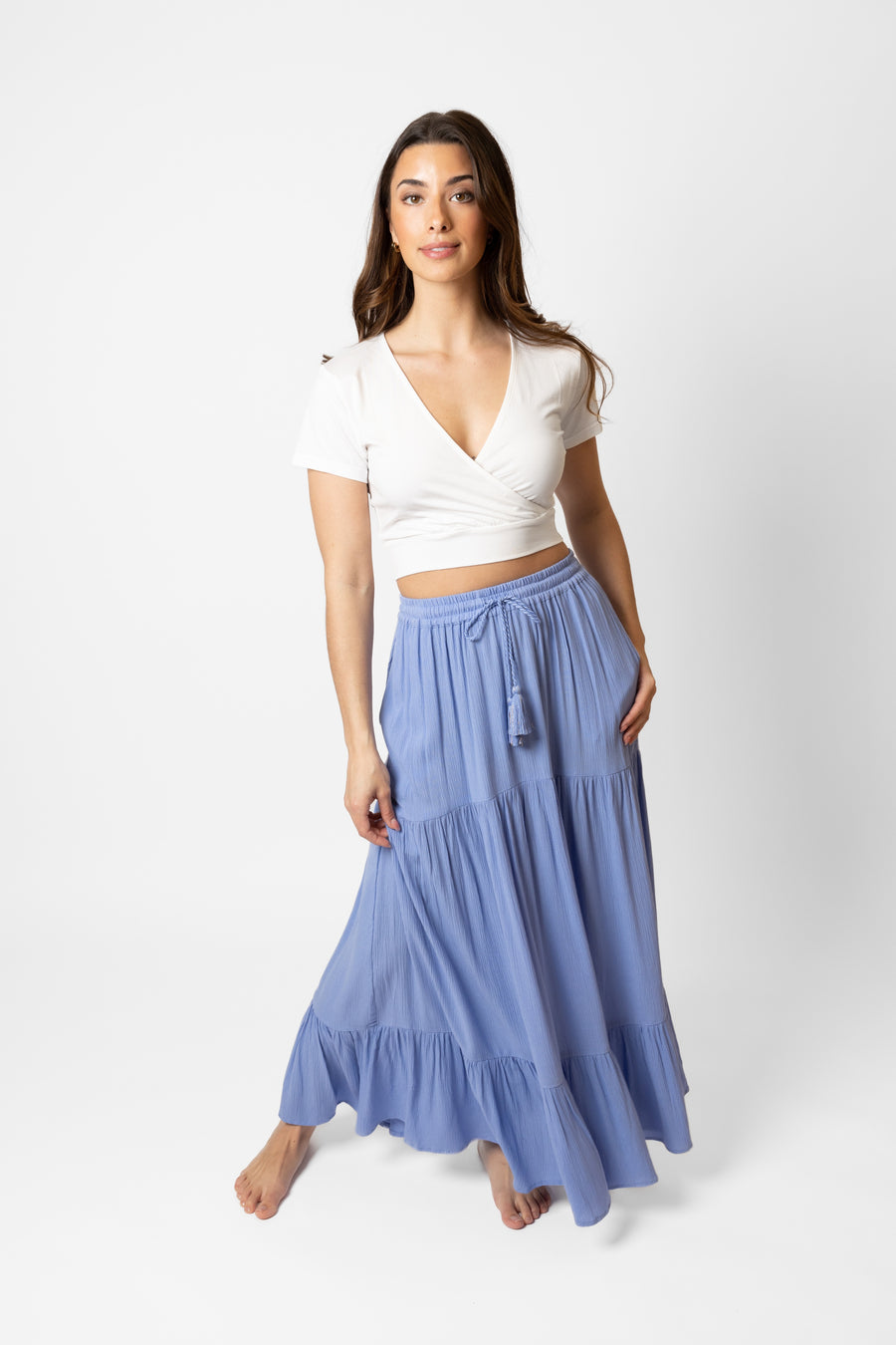 Brunette model facing front, wearing Bahama Blue Miami Tiered Boho Maxi Skirt with a flowy fit, adjustable elastic waistband and beaded drawcord, pockets, and white lining. Made from crinkle rayon. Perfect for bohemian beach days and romantic getaways. Koy Resort affordable vacation, cruise, and resort-wear.