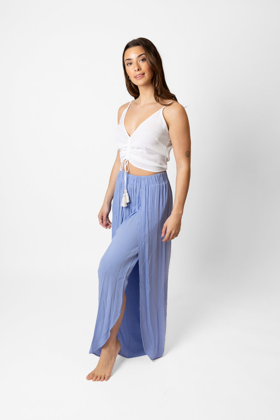 Brunette model facing side, wearing Bahama Blue Miami Split Leg Beach Pants made from crinkle rayon with an elastic waistband, high side slits, and rounded hem. Flowy yet true to size, perfect for a stylish and comfortable summer look. Koy Resort affordable vacation, cruise, and resort-wear.