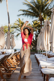 A brunette hair woman model wearing raspberry Miami collection tie front buttoned up top from Koy Resort and white Zuma Crochet Beach shorts from Koy Resort. Brunette model facing front, wearing a Raspberry Miami Tie Front Top. This vivacious top features chrome embellishments, a collar, and a tied knot in the front, blending sass and sophistication. It has a fitted top with a loose bodice, an adjustable front tie, and a button front. A best seller for daring yet sophisticated looks. Koy Resort affordable.