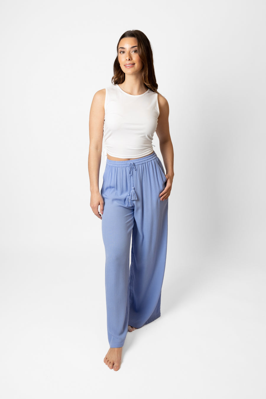 Brunette model facing front, wearing Bahama Blue Miami Wide Leg Pant with a flowy straight leg, elastic waist, side pockets, metallic tassel drawcord, and white lining. Palazzo style for a fun and flattering fit. Koy Resort affordable vacation, cruise, and resort-wear.