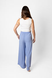 Brunette model facing back, wearing Bahama Blue Miami Wide Leg Pant with a flowy straight leg, elastic waist, side pockets, metallic tassel drawcord, and white lining. Palazzo style for a fun and flattering fit. Koy Resort affordable vacation, cruise, and resort-wear.