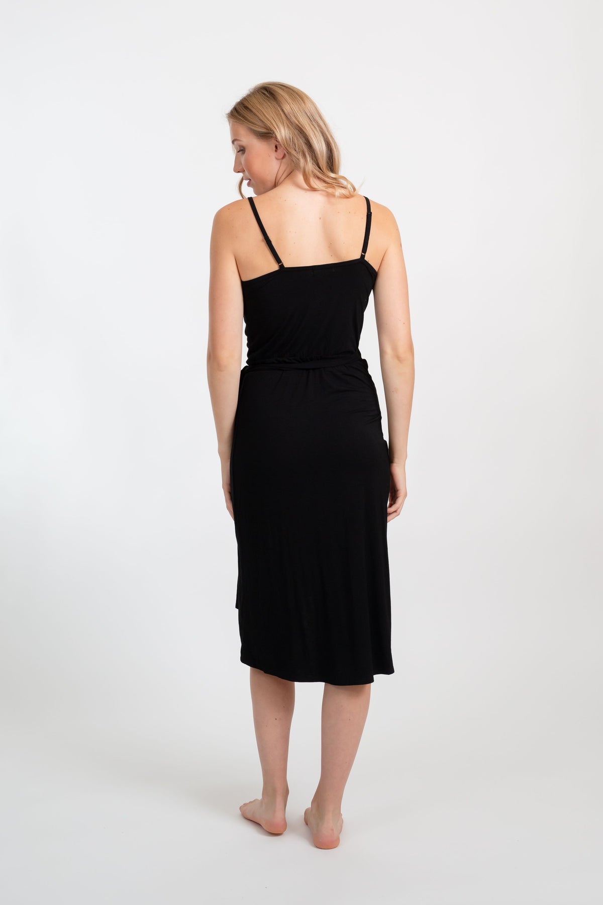 the back of a blonde hair female model wearing a black thin strap dress looking down