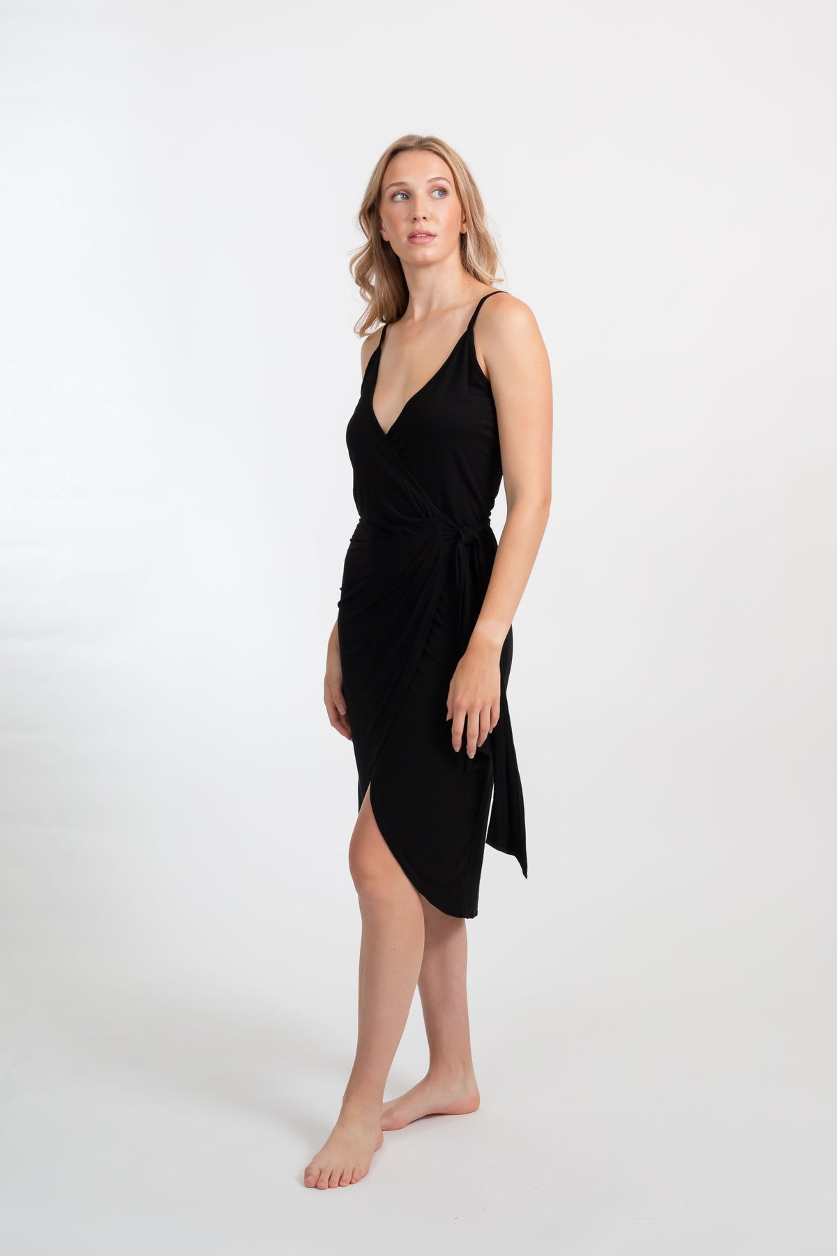 a blonde hair female model showing the side of the black spaghetti strap dress from Koy Resort looking up