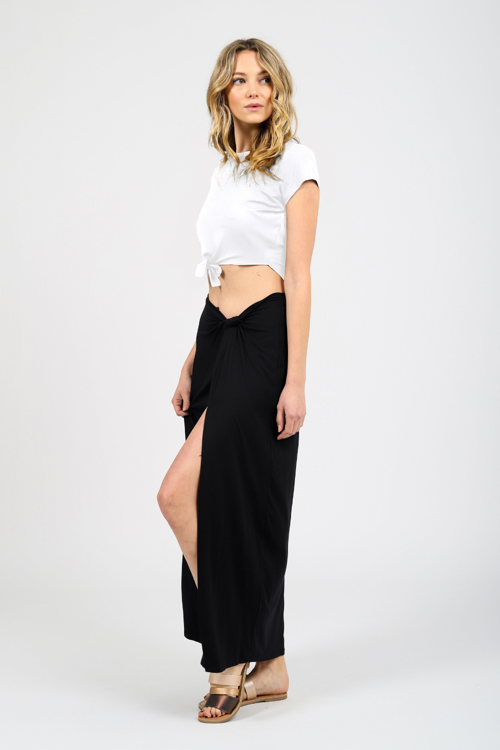 Blonde model wearing black laguna side knot maxi slit skirt facing side. Paired with Laguna knot top in white from Koy Resort. Koy Resort vacation cruise wear.