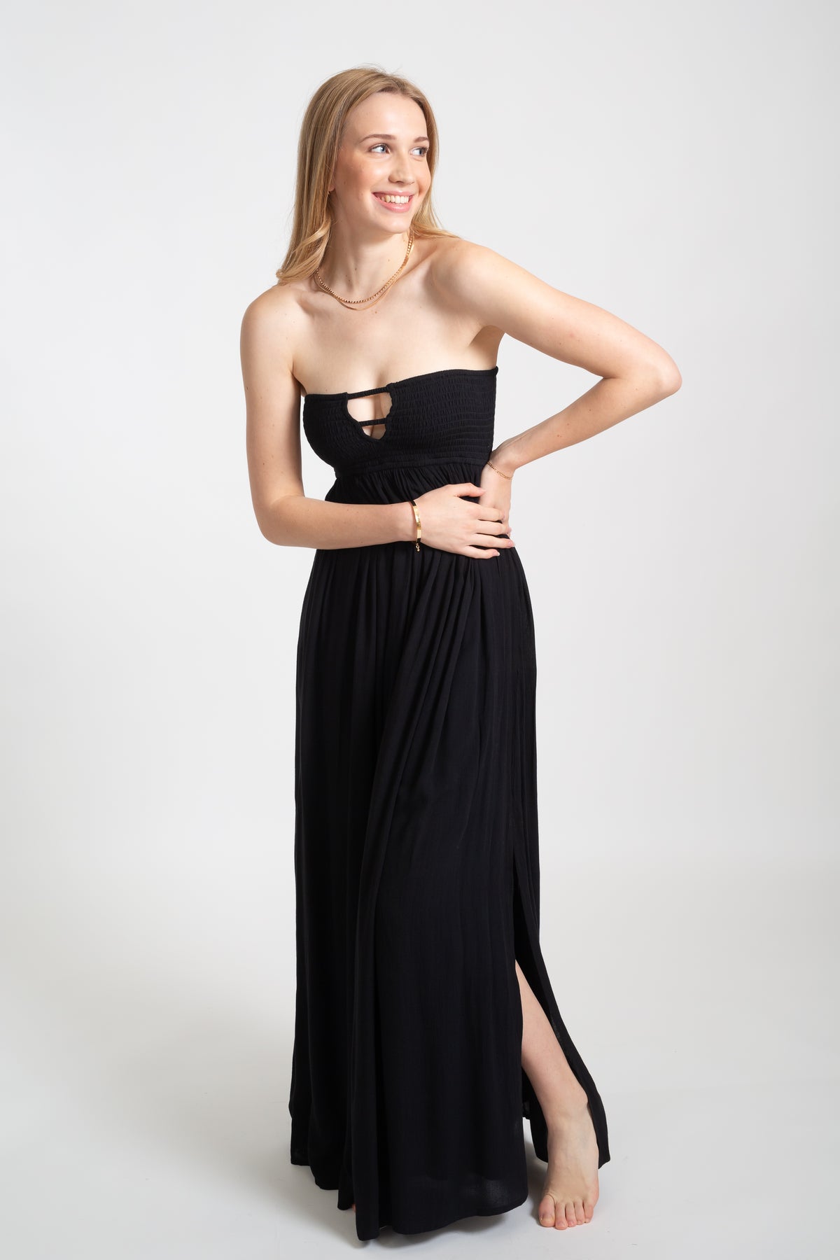 Blonde model wearing the black Miami maxi bandeau dress with the slit by Koy Resort Beachwear collection facing front. 