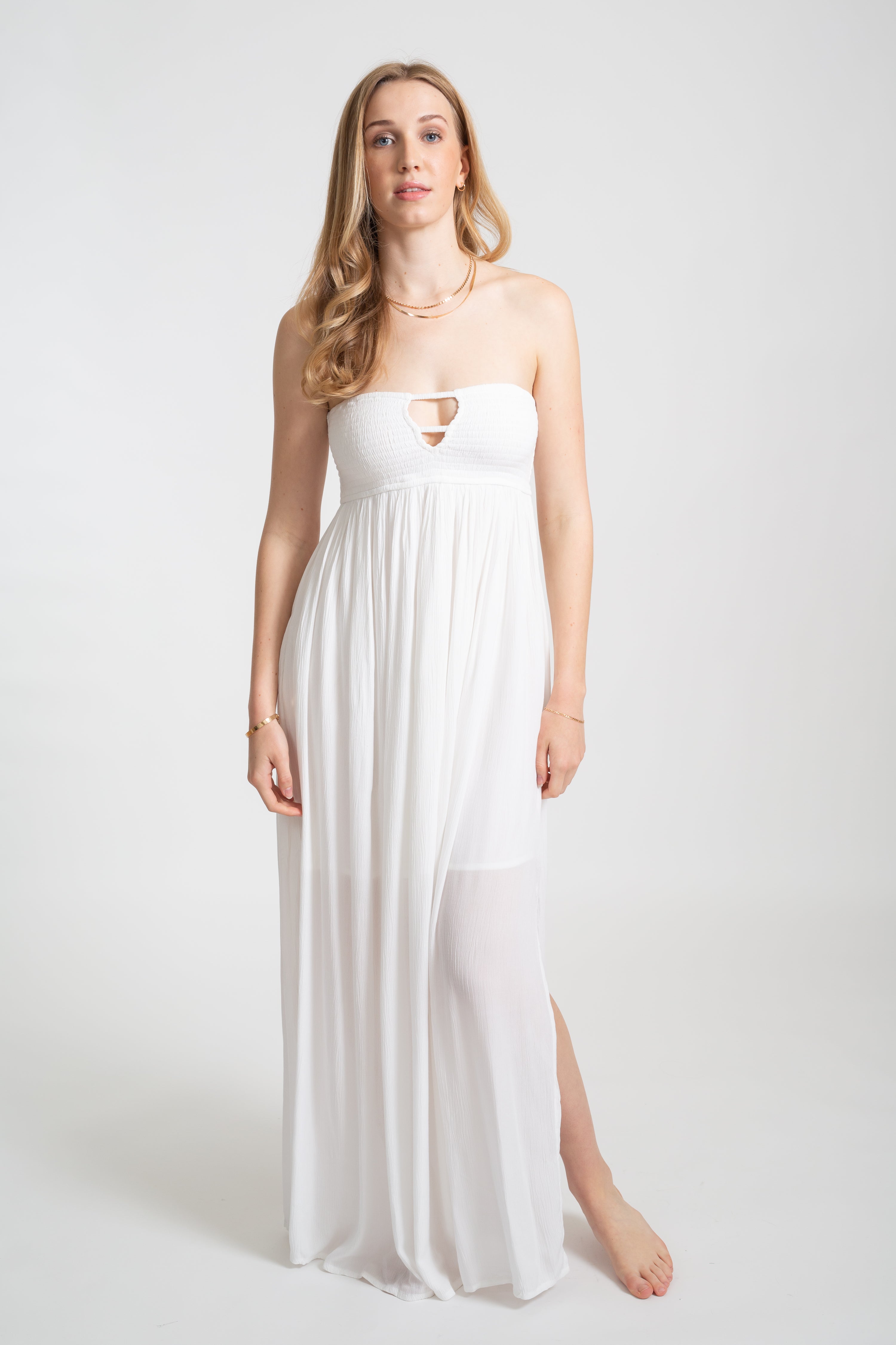 Blonde model wearing the white Miami maxi bandeau dress with the slit by Koy Resort Beachwear collection facing front.