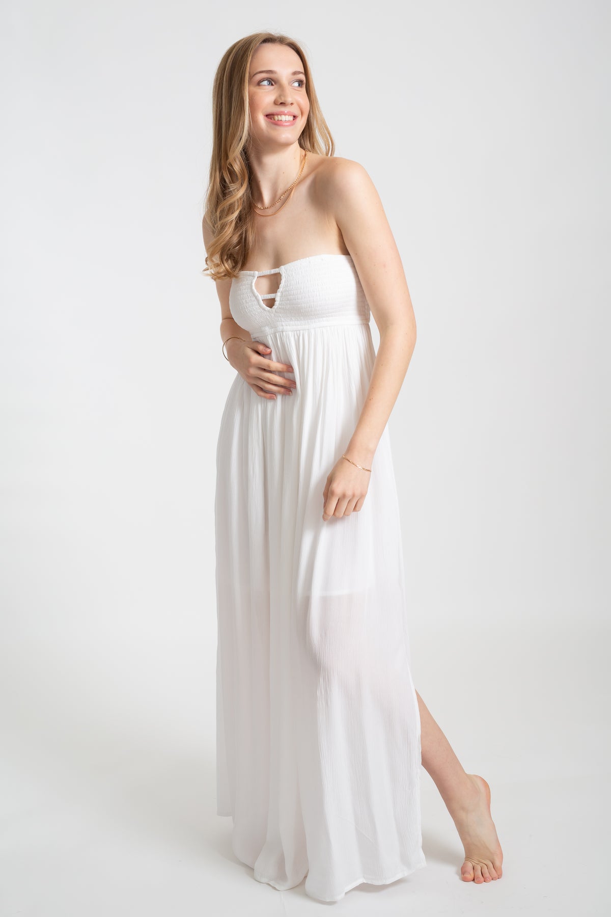 Blonde model wearing the white Miami maxi bandeau dress with the slit by Koy Resort Beachwear collection facing front. 