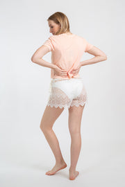 Koy Resort vacation, resort and beachwear. Model facing back wearing white cream lace flamenco shorts with adjustable waist tassel detail, paired with blush pink essential cropped crew neck tee