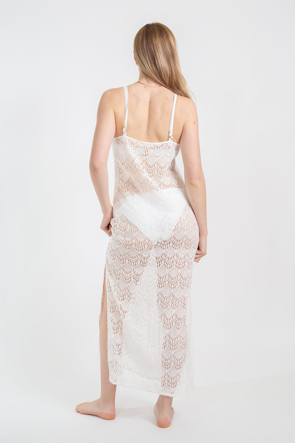Koy Resort vacation, resort and beachwear. Model facing back wearing white cream lace flamenco cover up midi dress with adjustable spaghetti straps and slits