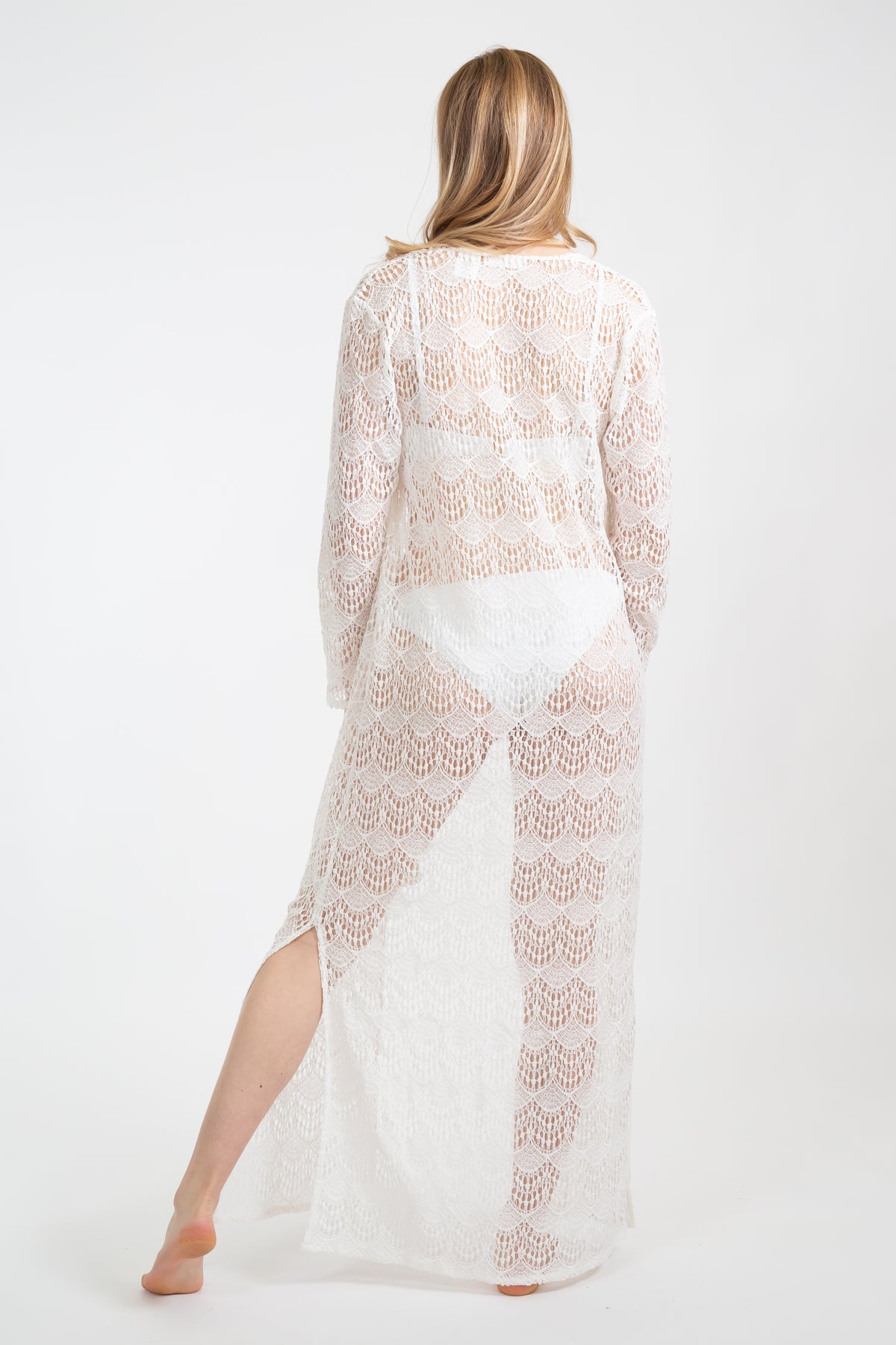 Koy Resort travel and beach wear. Long white flamenco collection cardigan on model facing from. Featuring long sleeves in white lace with tassles. 