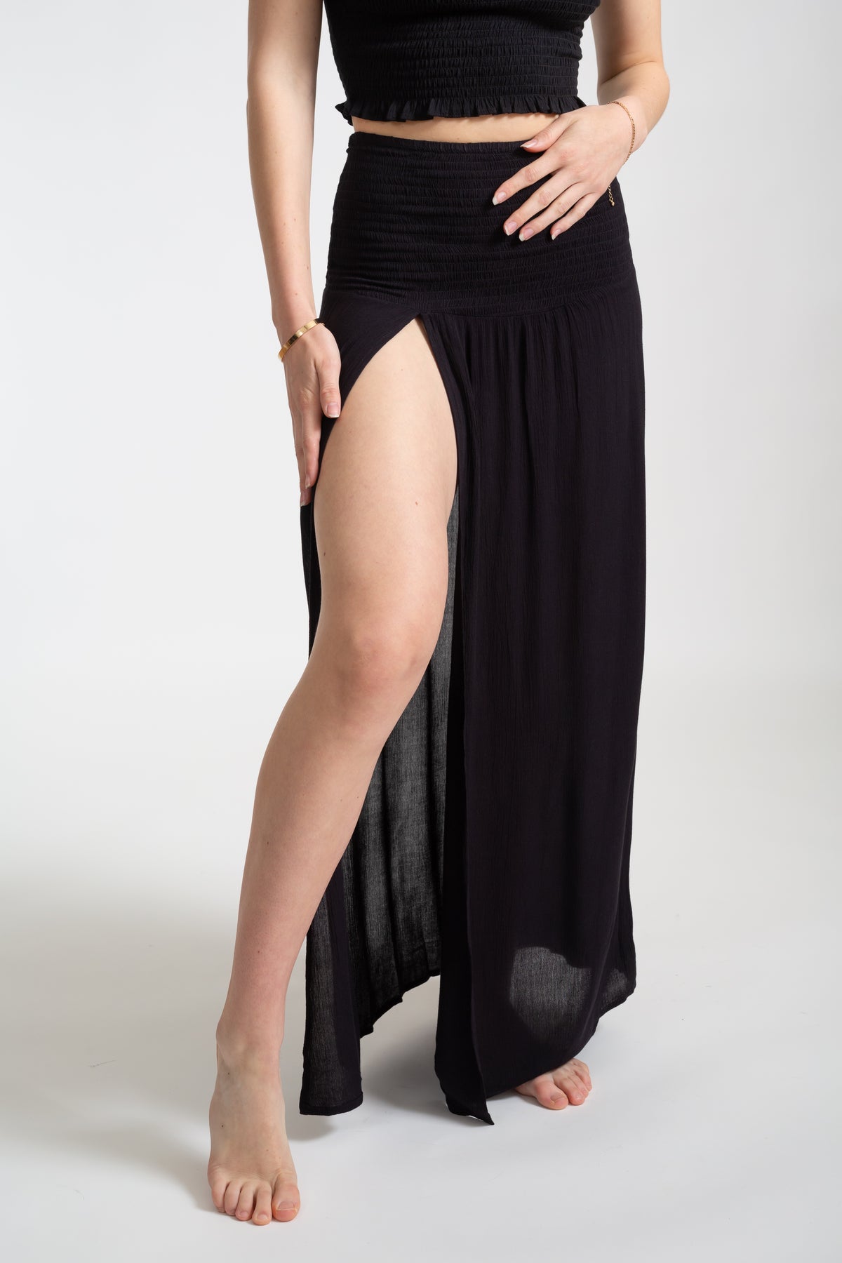 Blonde model wearing the black Miami convertible skirt with deep slit facing front close up. Featuring smocked detailing, fabric is hundred percent crinkle rayon by Koy Resort cover-up summer collection.