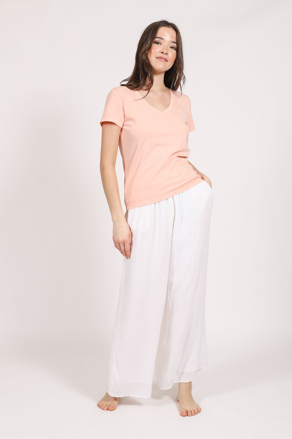 Brunette model wearing the white Miami crop pants with crinkle rayon fabric facing front. Paired with the blush essentials t-shirt by Koy Resort Summer Collection. 