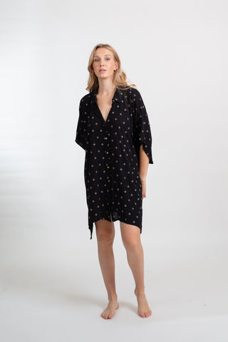 the front shot of a blonde hair woman model wearing a black with gold dot printbig shirt dress with her hands behind her back