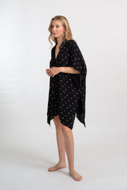 a side shot of a blonde hair female model wearing an oversized black with gold dot print shirt dress