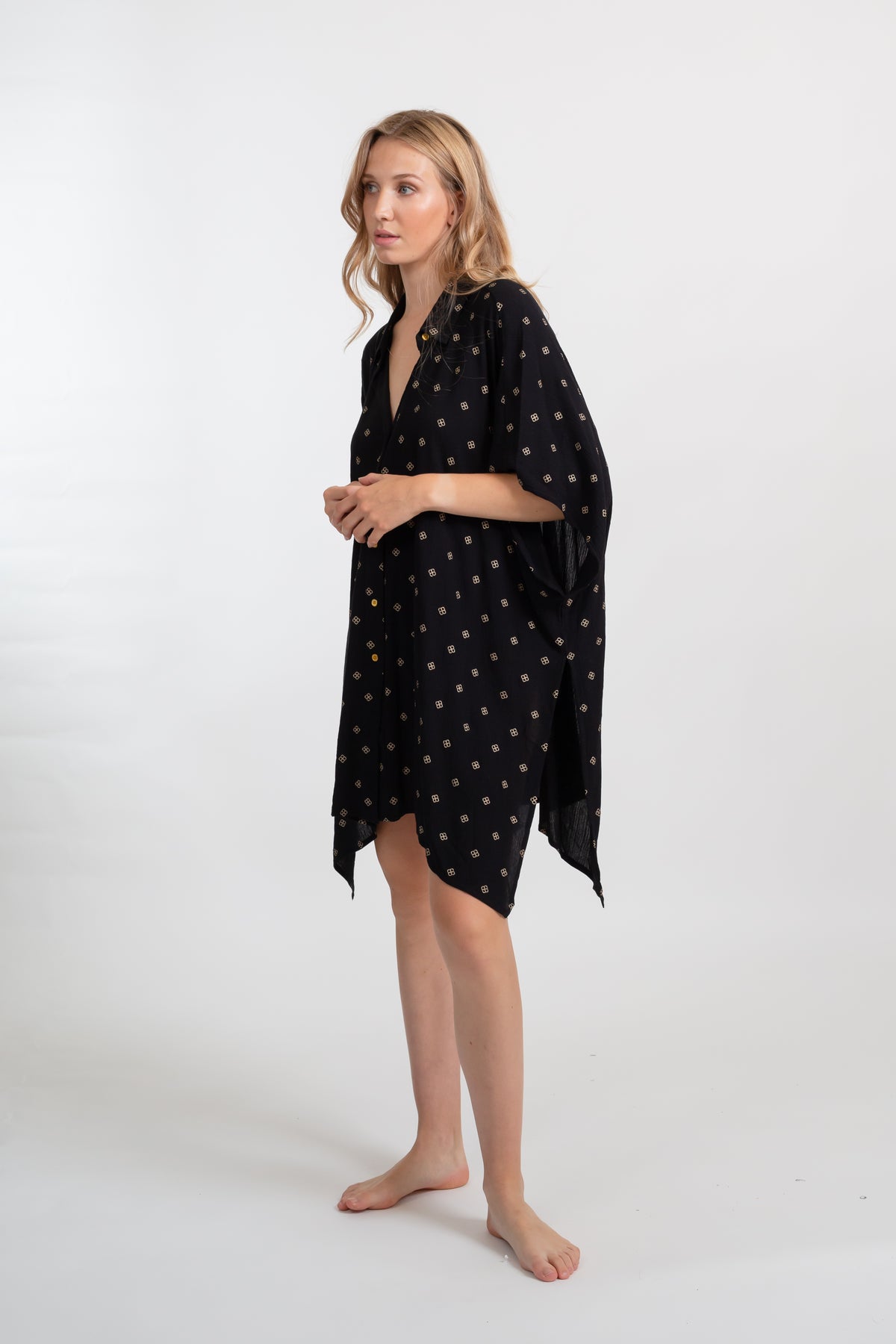 a side shot of a blonde hair female model wearing an oversized black with gold dot print shirt dress