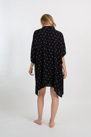 the back of a blonde hair woman model looking down wearing a black with gold print big shirt dress from Koy Resort