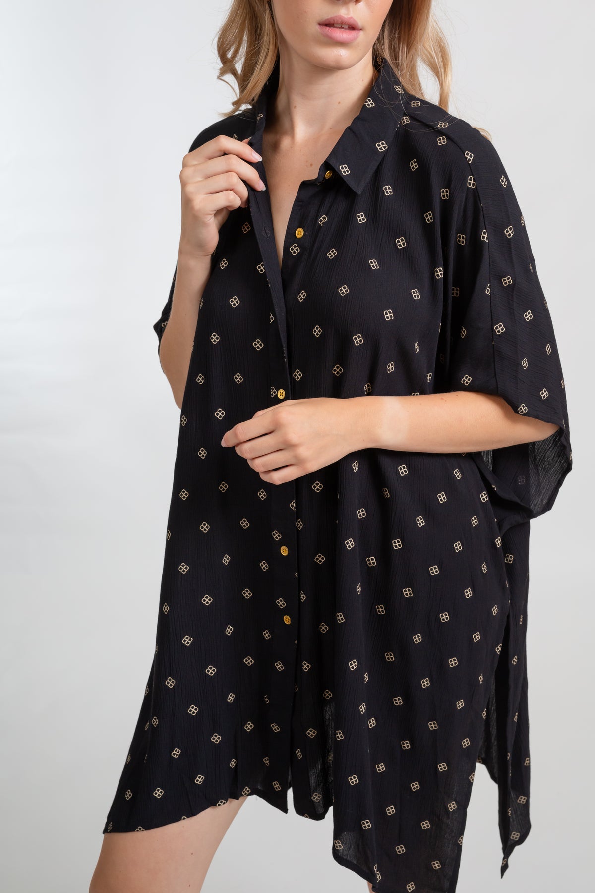 a zoomed in shot of a woman model wearing a buttoned up flowy black with gold dot print oversized shirt dress from Koy Resort