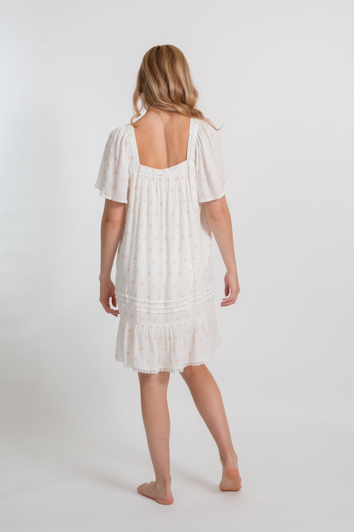 the back of a blonde hair woman wearing white with gold dot print vacation style beach dress