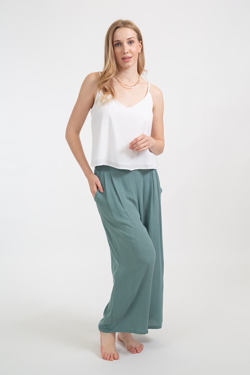 Blonde model wearing the white soft Miami Camisole top with adjustable straps and v-neckline facing front. Paired with crinkle rayon jade green Miami pants by Koy Resort Cruise summer beachwear collection.