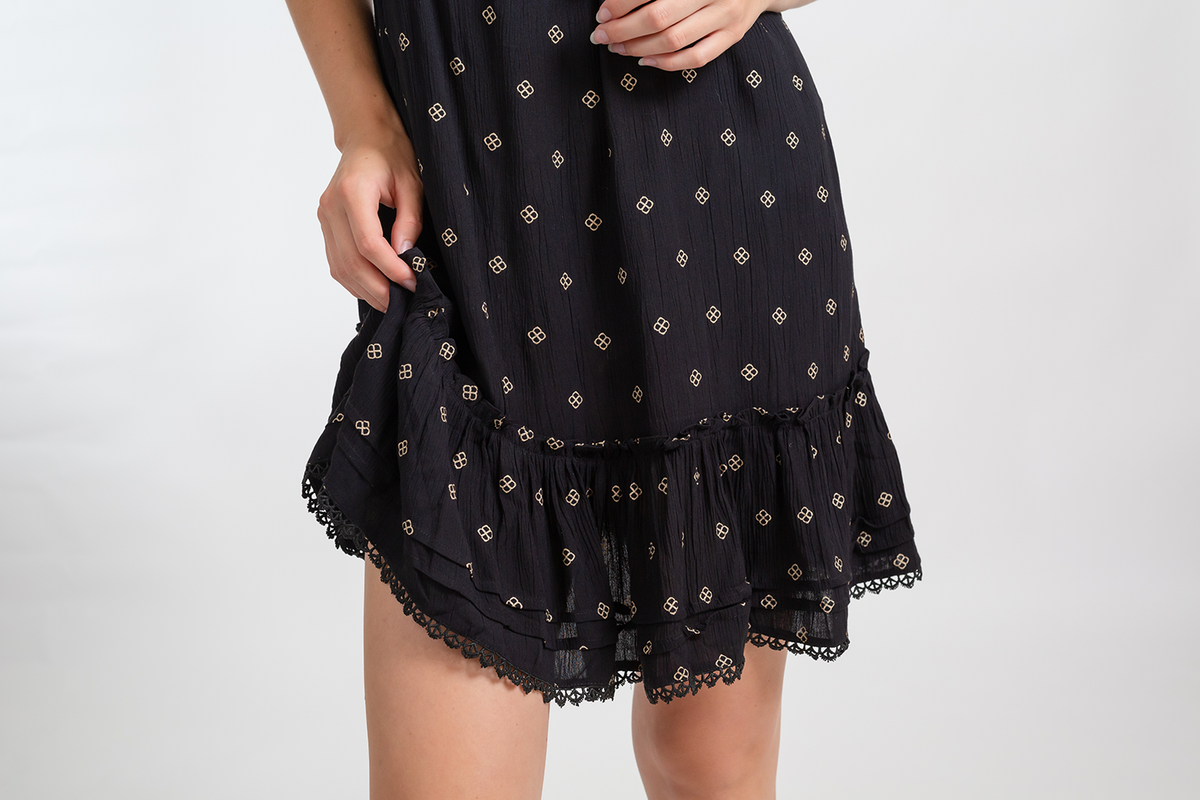 a zoomed in of a black with gold dot print beach dress showing the flowy fabric