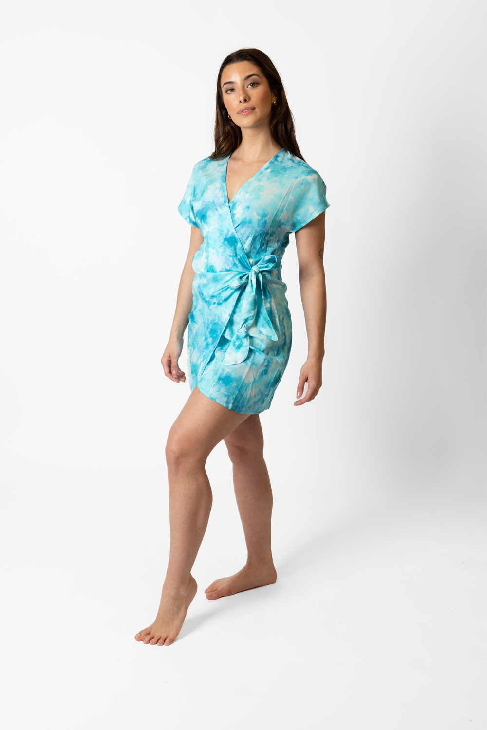 A woman in a blue tie-dye mini dress showing the knot on the side of her waist posing a confident and carefree attitude