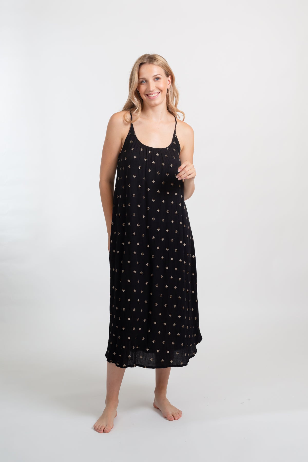 a blonde hair woman model facing front wearing a black with gold dot print vacation style midi dress smiling