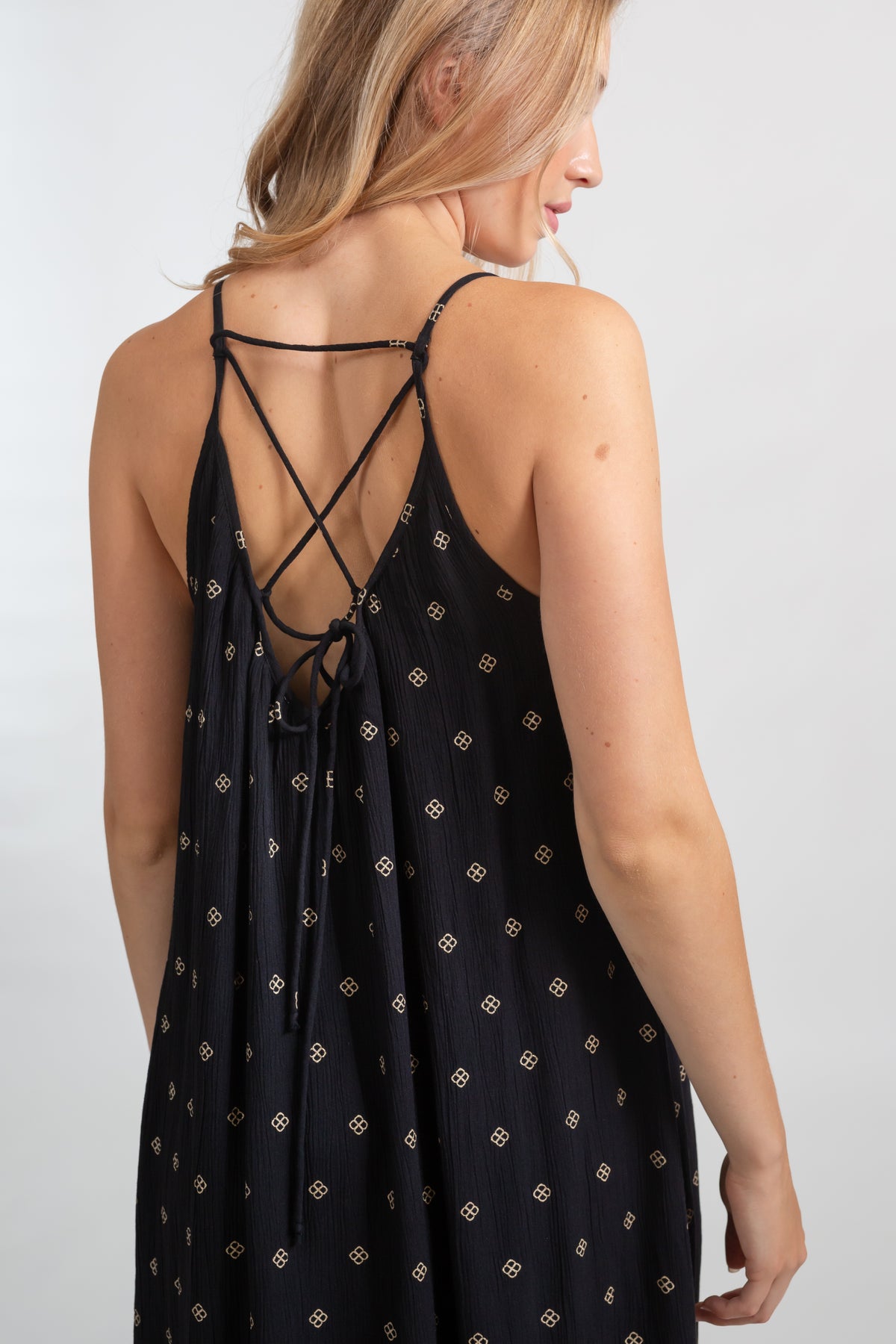 the back of a blonde hair female model wearing a black with gold dot print design strappy dress