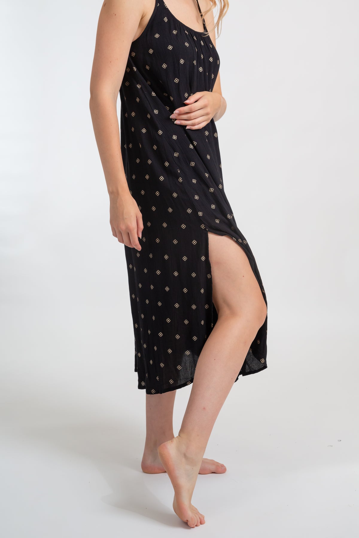 a zoomed in shot of a woman model wearing a black with gold dot print midi dress with a slit on the side