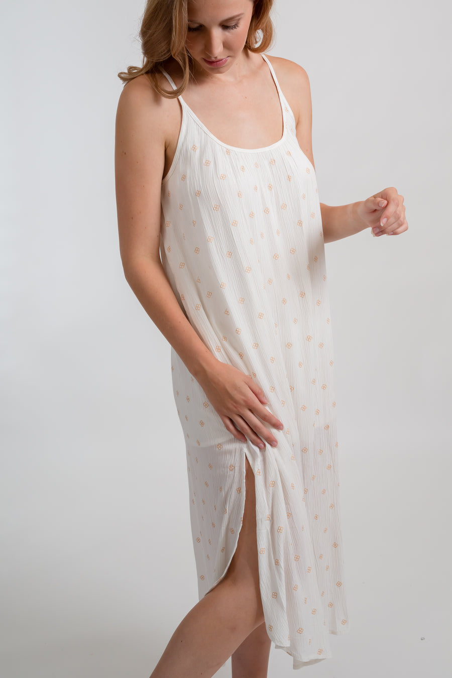 a blonde hair women model wearing a white strappy midi dress with side slit and gold dot print looking down