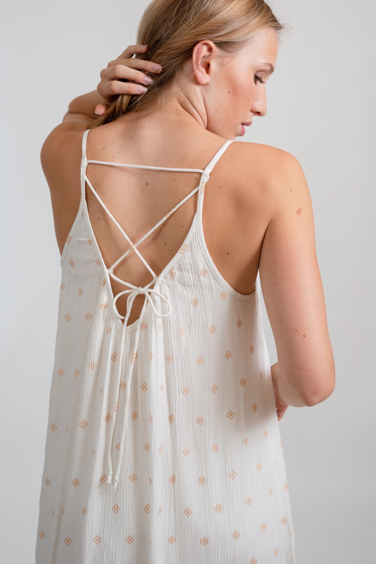 the back of a blonde hair model wearing a strappy vacation feel white with gold dot print dress looking to the side