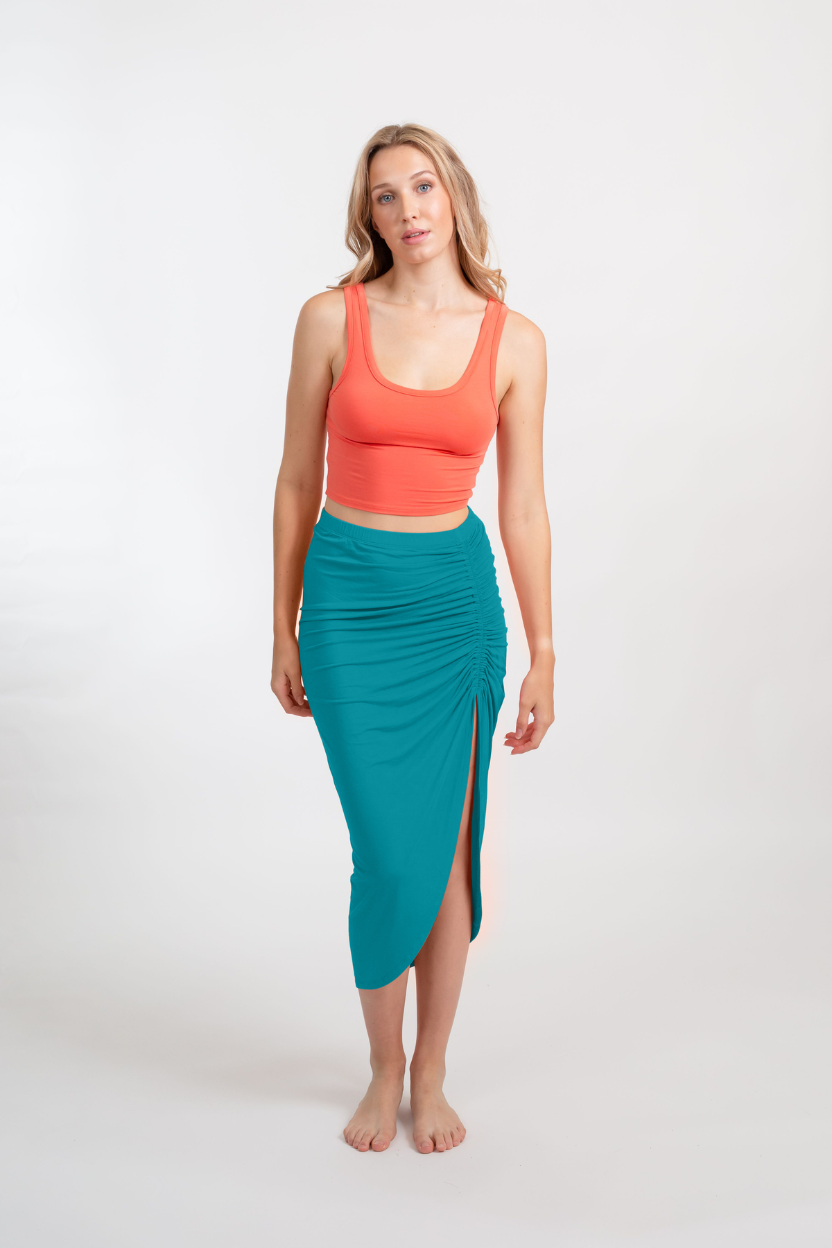 a blonde hair female model facing front wearing a coral punch tank top and and an auqa colored side slit midi skirt