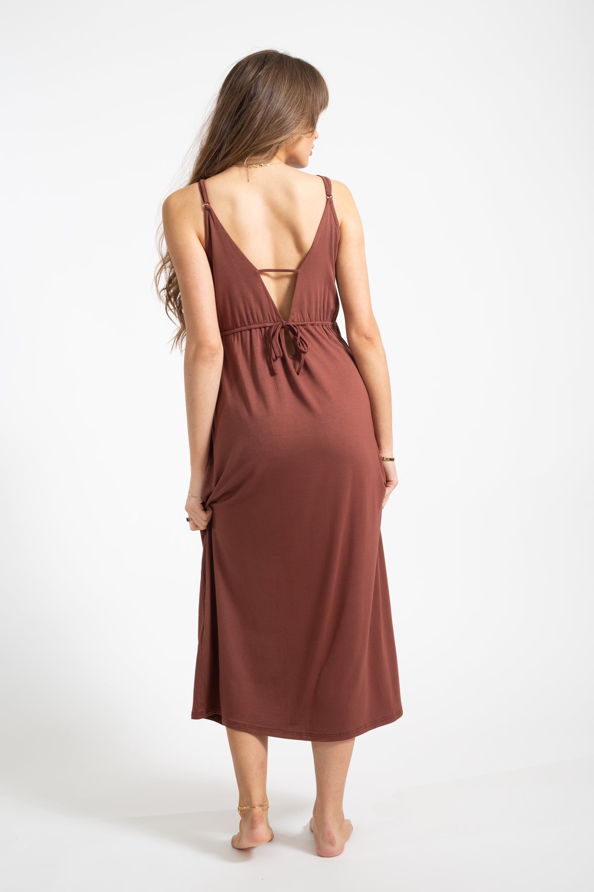 Brunette model wearing Mocha Brown Laguna Cotton deep-v neck strappy midi dress with side slit facing  the back. Koy Resort affordable vacation, cruise and resort-wear
