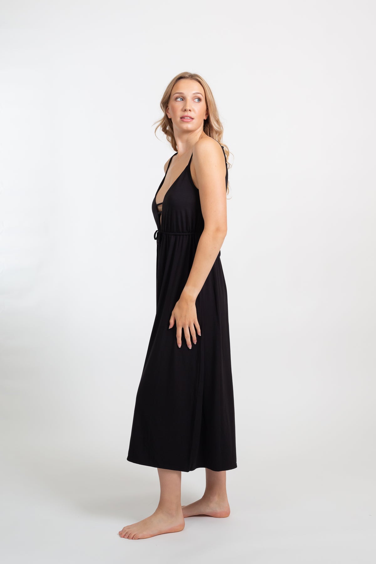 Blonde model wearing Black Laguna Cotton deep-v neck strappy midi dress with side slit facing side. Koy Resort affordable vacation, cruise and resort-wear.