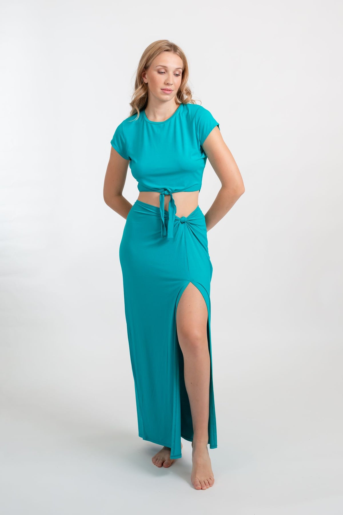 a blonde hair women model wearing a matching auqamarine color crop shirt and side knot maxi skirt with a side slit