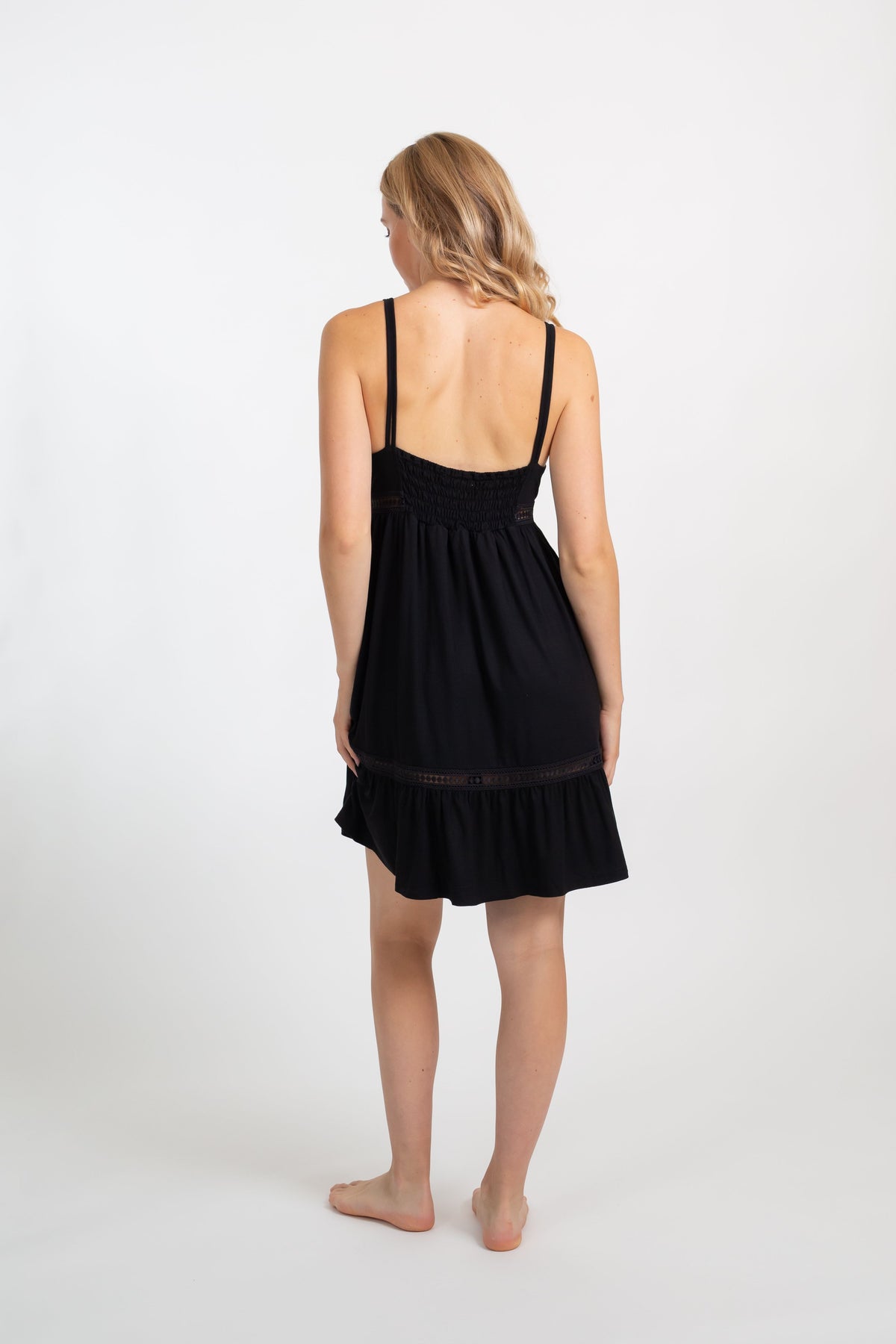 the back of a blonde hair model wearing a black adjustiable strappy black mini dress from Koy Resort
