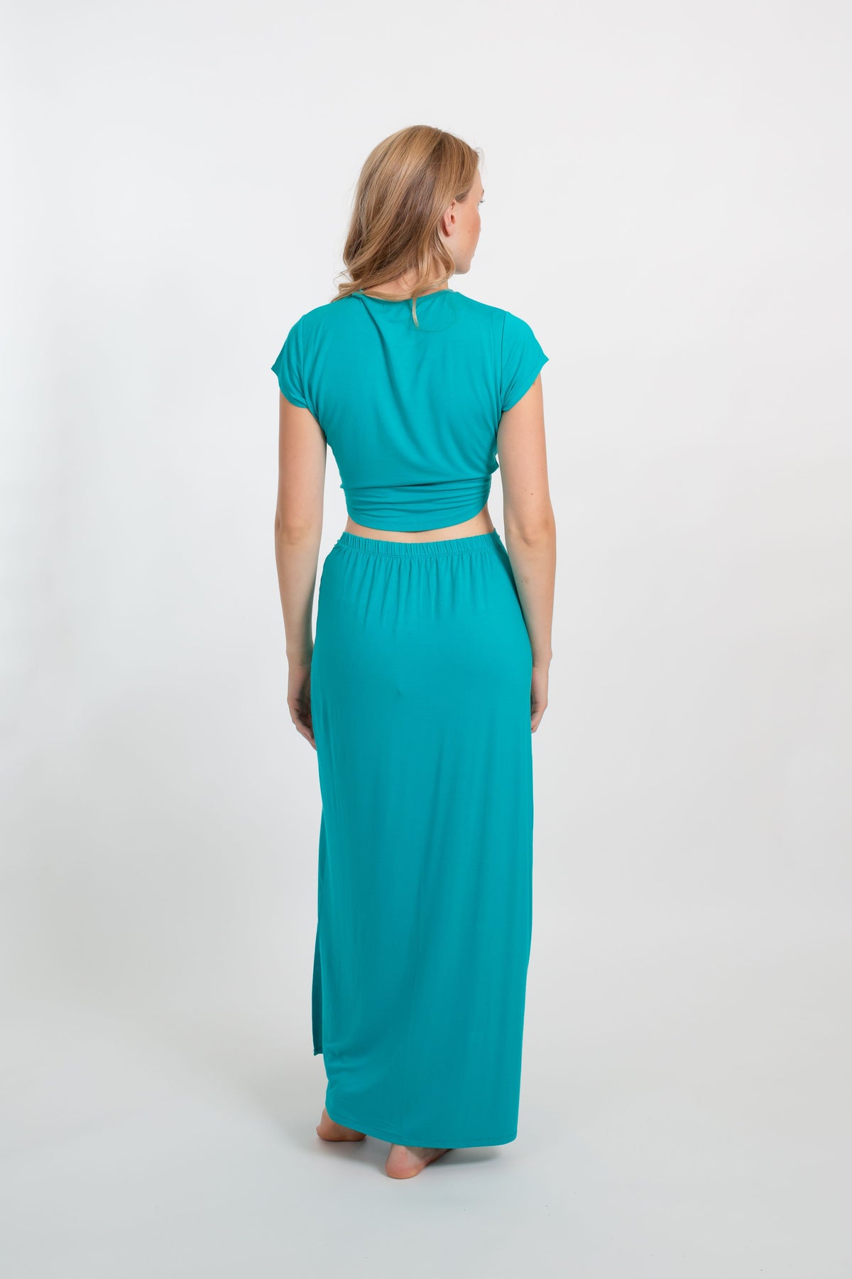 the back of a blonde hair woman model wearing matching crop top and maxi skirt in the color auqamarine fro Koy Resort