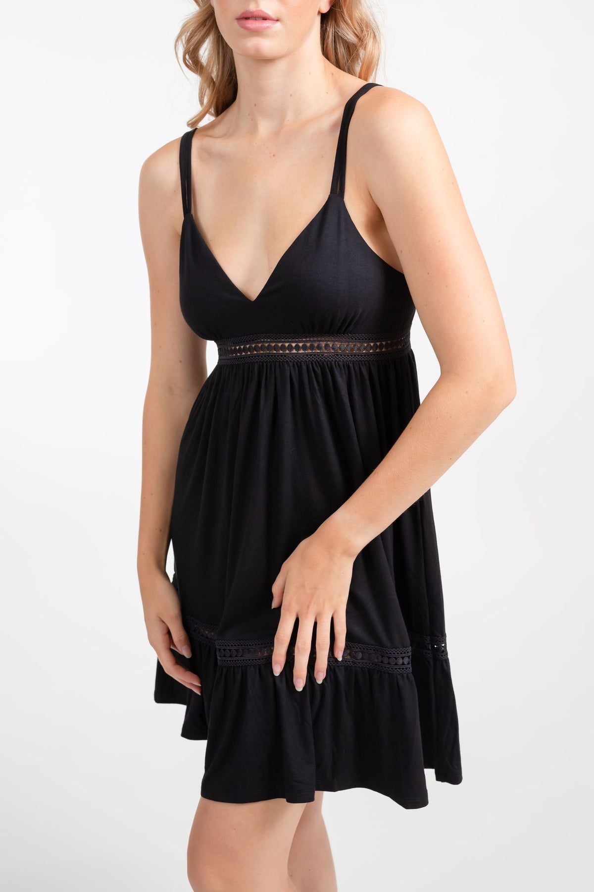a zoomed in shot of a blonde hair women model wearing a black strappy v-neck crochet trim dress with both hands in the front