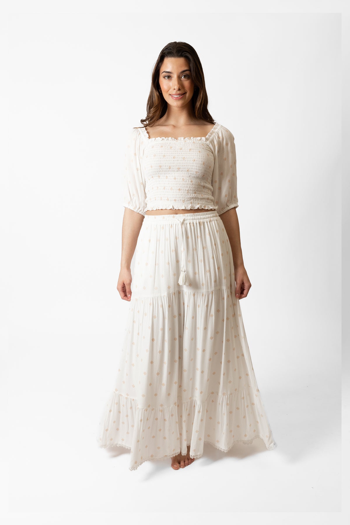 a front shot of a brunette hair woman wearing white with dot print matching crop top and maxi skirt smiling
